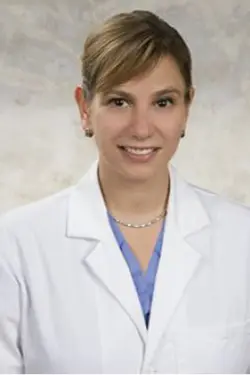 Headshot of a medical professional, she smiles at the camera, she has her hair up, and has on a white coat