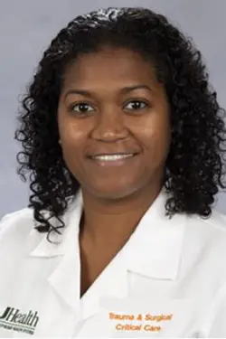 Headshot of a medical professional, she smiles at the camera, she has curly dark short hair, and has on a white coat