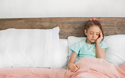 girl lying in bed holding her head with a pained face