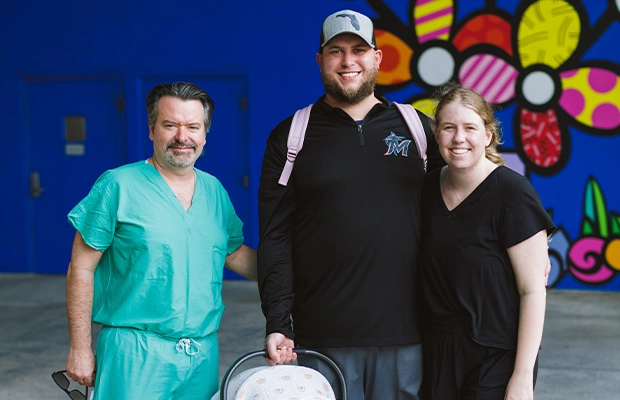 A couple embracing and lifting up their son, posing and smiling next to a doctor.