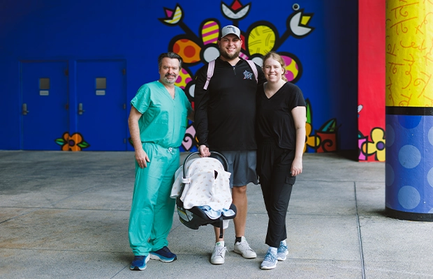 A couple embracing and lifting up their son, posing and smiling next to a doctor.