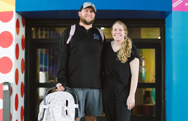 A couple posing for the camera in front of the hospital while holding their baby.