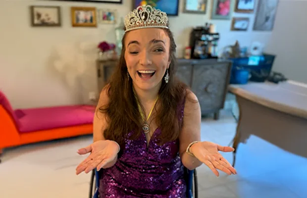 woman sitting in wheelchair wearing purple sparkly dress with silver crown