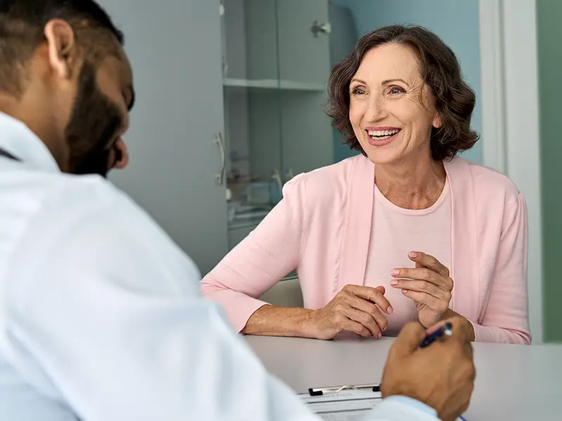 A patient speaking to a medical professional in a medical center, she smiles towards her physician