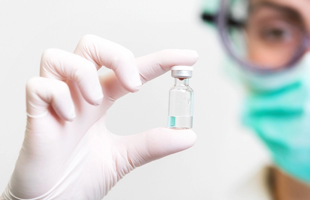 Close-up of a hand with surgical gloves showing a small bottle of medicine