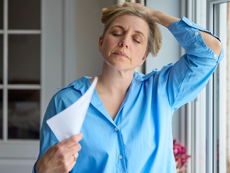 Blonde adult woman in blue t-shirt holding her head as if it hurts