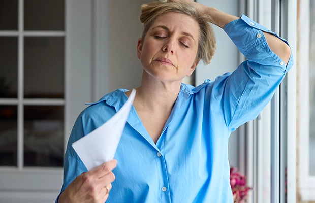 Blonde adult woman in blue t-shirt holding her head as if it hurts