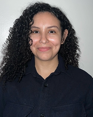 Close-up of a woman with curly hair wearing a black t-shirt, smiling at the camera.
