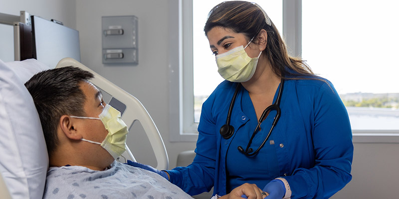 A medical professional looking down and holding the hand of a patient