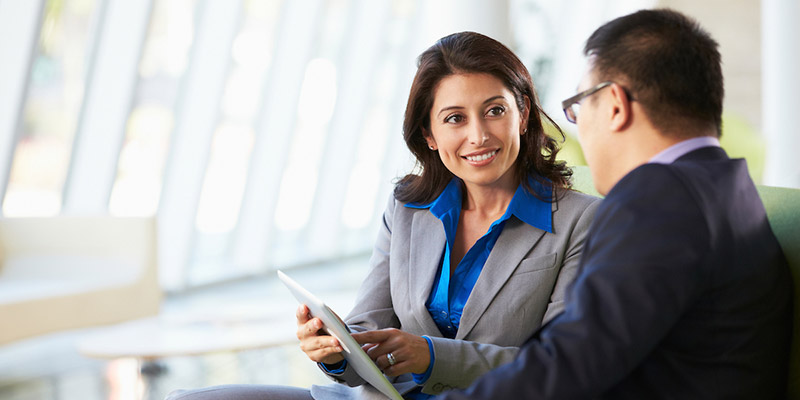 A professional woman sitting next to a man and showing him something on a tablet