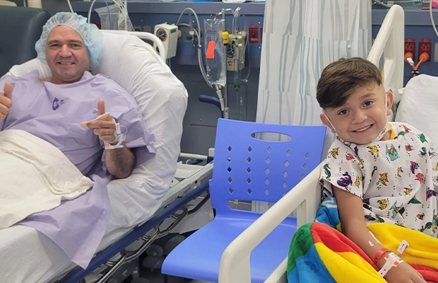 Child lying on a hospital stretcher smiling next to a man beside him