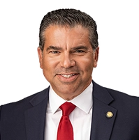 Close-up of a man in a suit and tie smiling at the camera against a white background.