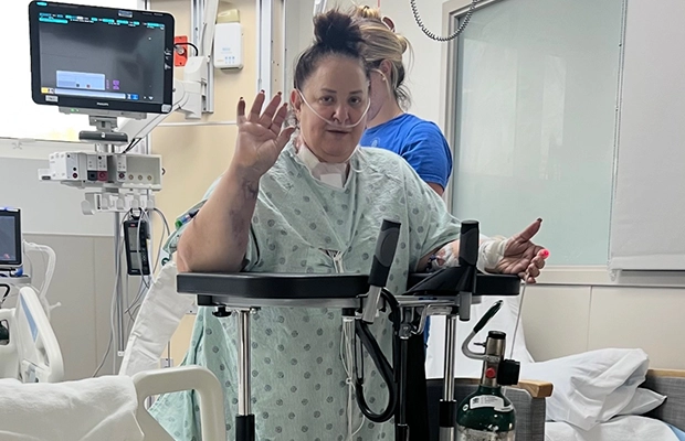 Woman walking with the help of a nurse in a hospital while waving to the camera