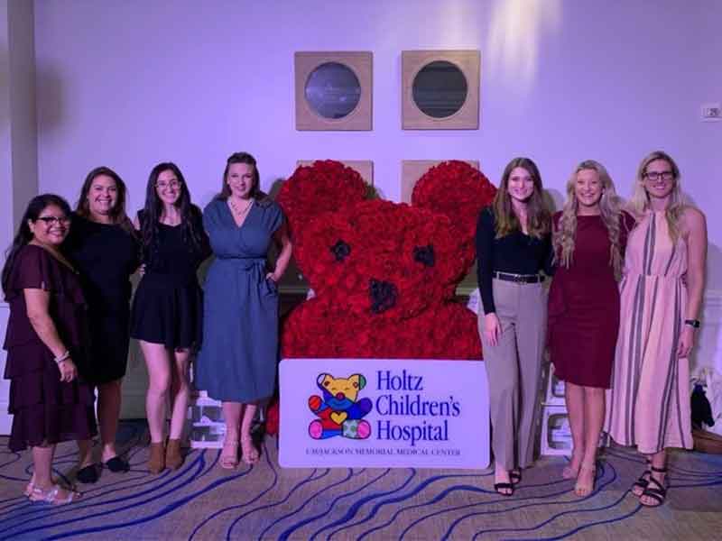 Group of women posing to the camera next to flower arrangement