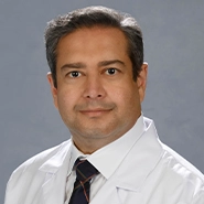 A headshot of a medical professional, he has on a white coat and dark tie