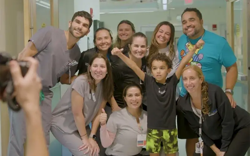 A group of medical professionals and a family smiling at a camera, they are standing within the hallway of a medical building