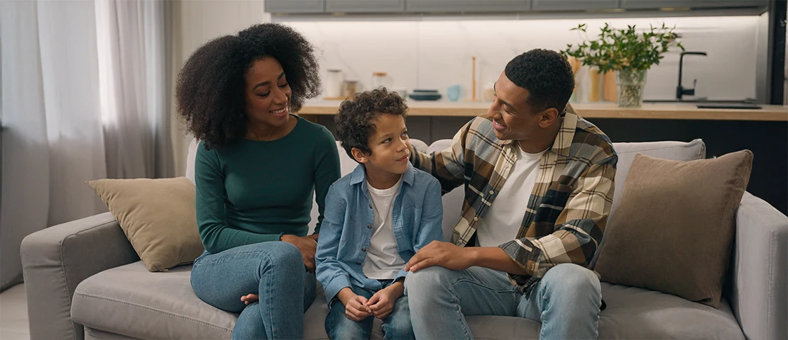 Two parents speaking with their child, they sit on a couch