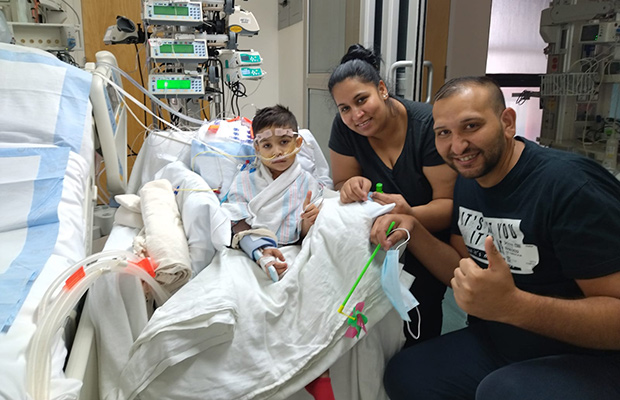 A young boy, man, and woman in a medical room, the young boy has medical devices around him