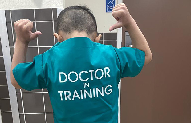 A closeup of a young boy's back, he is wearing a surgery costume that reads Doctor in Training