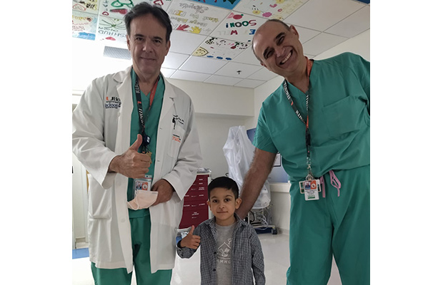 Two medical professionals and a young boy within a medical room, they all smile at the camera