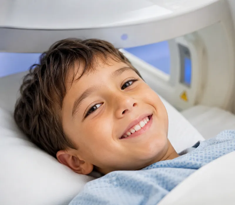 A young boy smiling at the camera, he is wearing scrubs