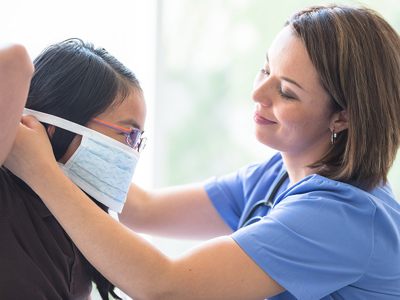 A physician placing a face mask on her young female patient