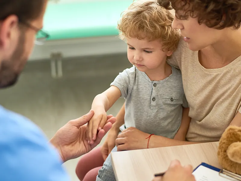 A physician checking a young child's arm as they sit on their moms lap