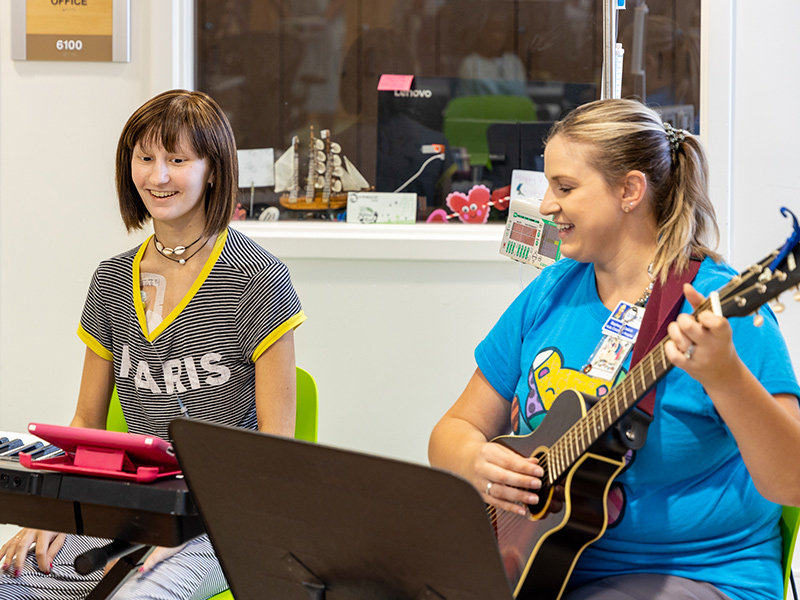 Young patient playing a piano next to a woman playing a guitar