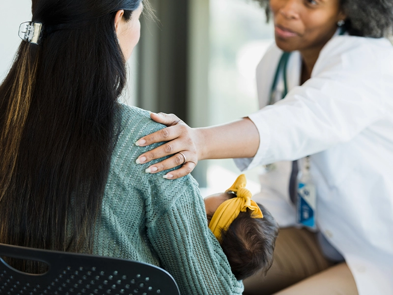 An image showing a doctor speaking with a woman holding her baby.