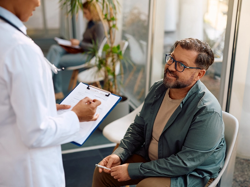 Man in a green blazer sitting in a doctor's office while talking to his doctor