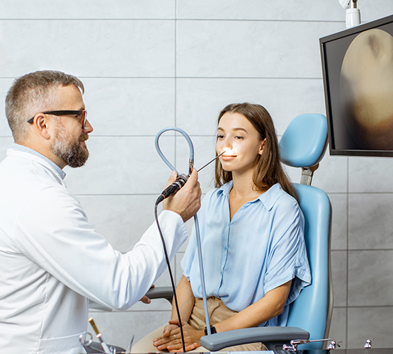 A physician making an endoscopic examination of a nose of a young female patient