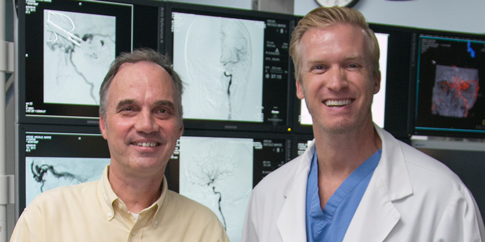Eric Keller and Doctor Peterson standing next to each other and smiling, they are standing in front of x-rays