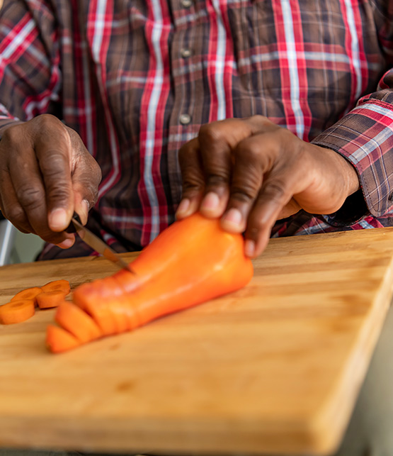 Closeup of a person in a wheelchair cutting up an orange bell pepper
