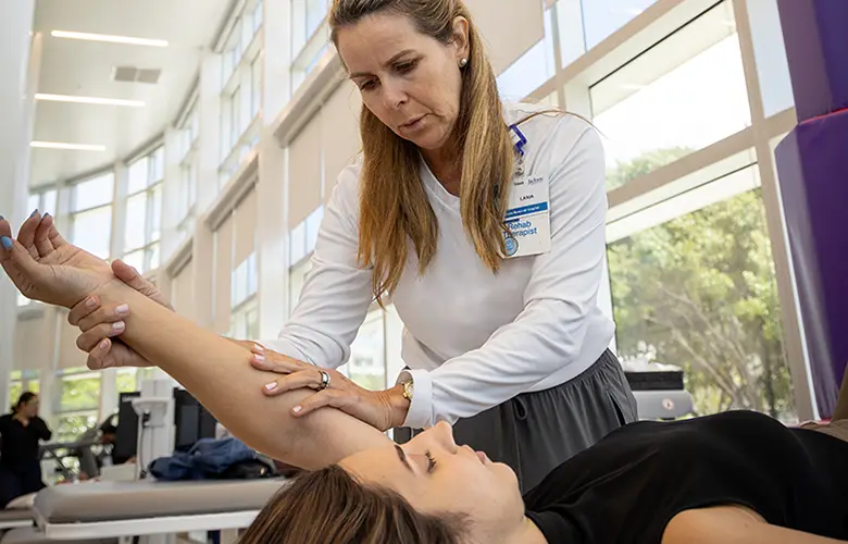 A physical therapist guides a patient through an arm stretch at a rehabilitation facility