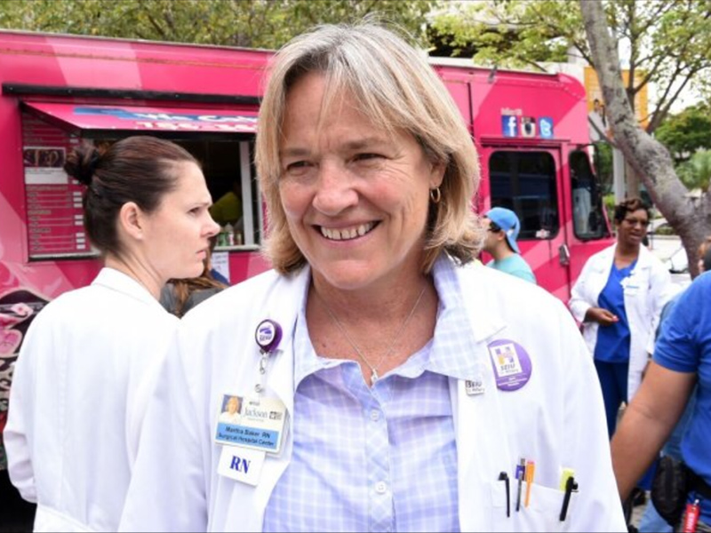 Martha smiling near a pink food truck, she has a white coat and a collared shirt on