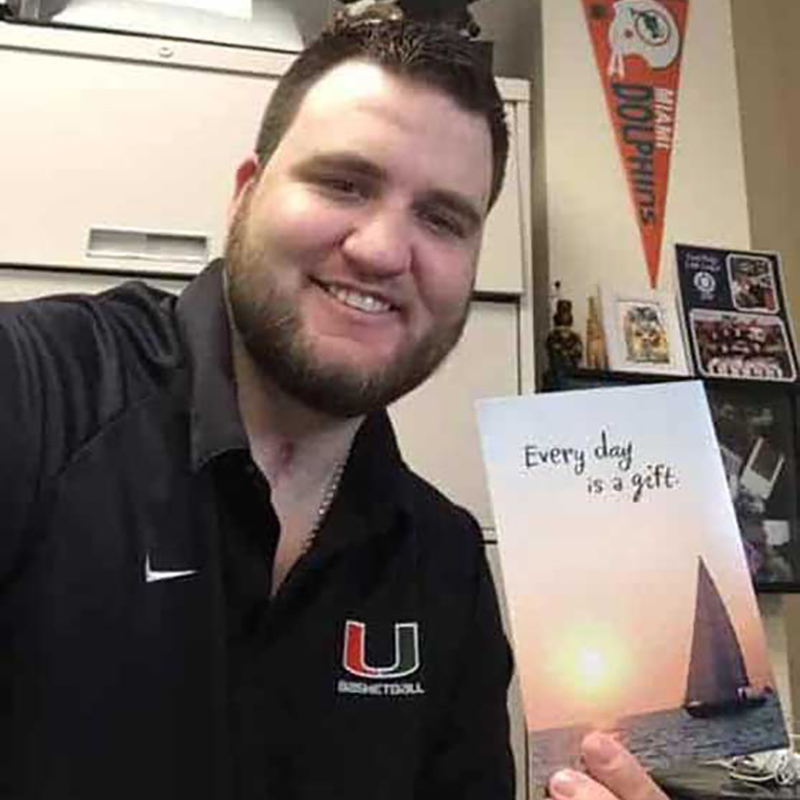 Chris Rotella looking and smiling at the camera while holding a piece of paper that says Every day is a gift.