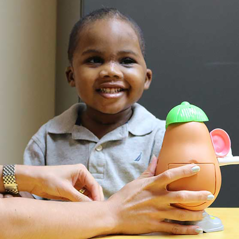 Darnal Mundy sitting and smiling as he sits across a Mr. Potato head