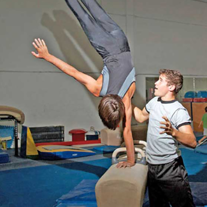 Jorge Valdes training a boy on a pommel horse, the child is holding up his body with one hand