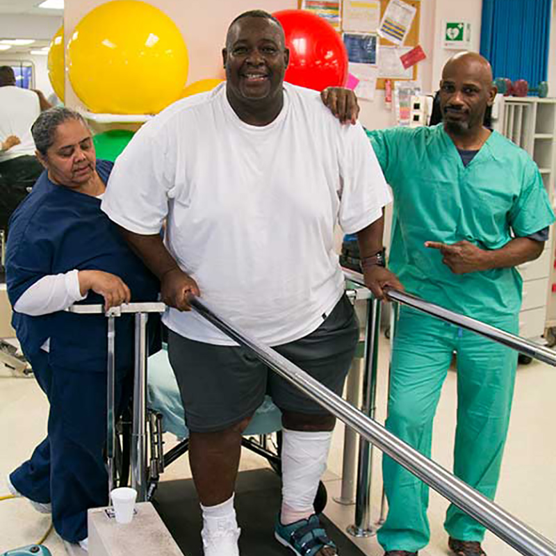 Robert Billue during a therapy session, two people are helping him walk