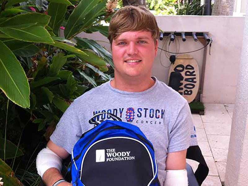 Woody sitting in his wheelchair, he's holding a backpack that says The Woody Foundation
