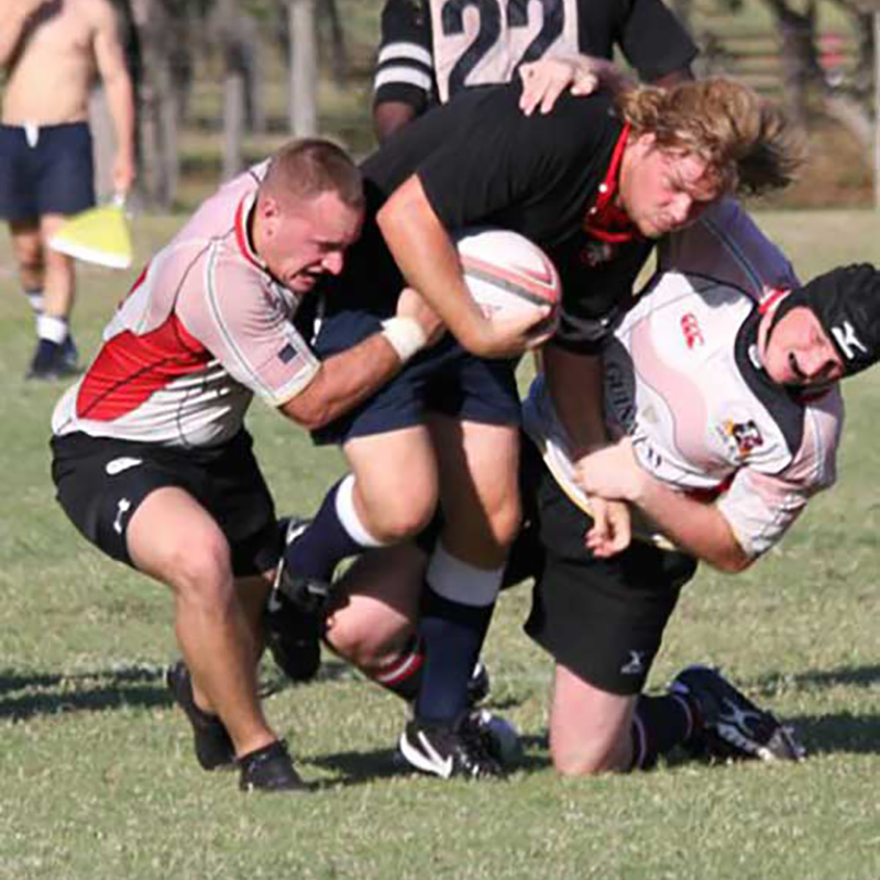 Woody playing rugby, he is being tackled as he holds the ball