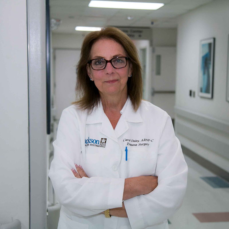 Carol standing in a hospital hallway, she's wearing a white coat and is smiling at the camera