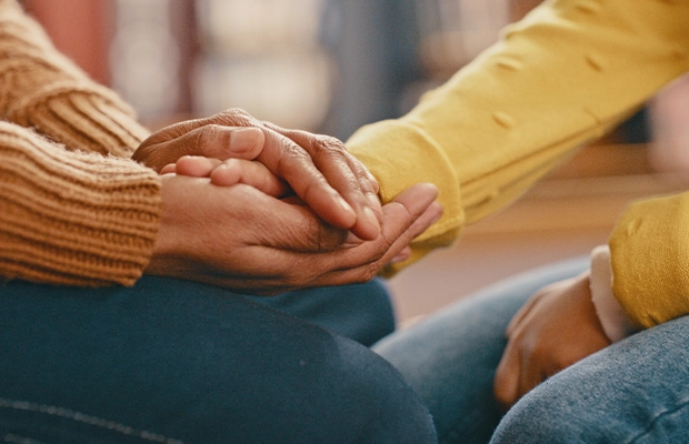 Close-up of two people holding hands, one dressed in beige and the other in yellow