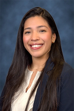 Close-up of a smiling woman dressed elegantly, with a blue background behind her.