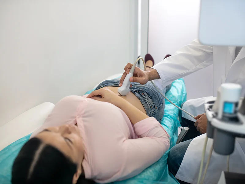 A doctor performs an abdominal ultrasound on a woman lying on a medical examination table.