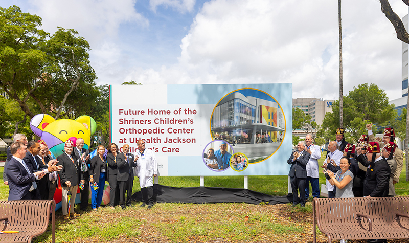 A group of people standing outdoors and clapping, they are standing in front of a billboard