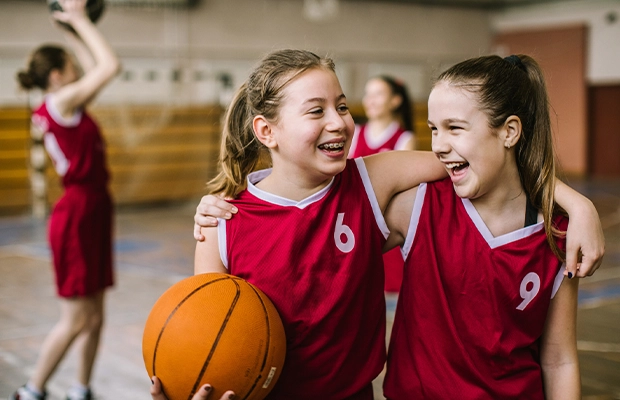 Two girls dressed in basketball uniforms in the middle of the court hugging each other