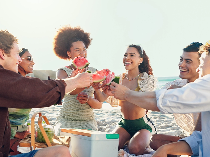 A group of people celebrating on the beach with slices of watermelon in their hands.