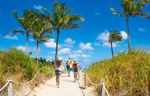 A photograph of a landscape featuring sand, the sea, palm trees, and a very blue sky.