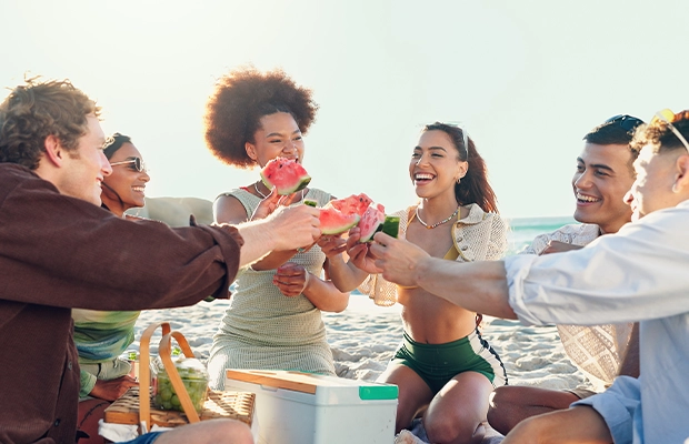 A group of people celebrating on the beach with slices of watermelon in their hands.